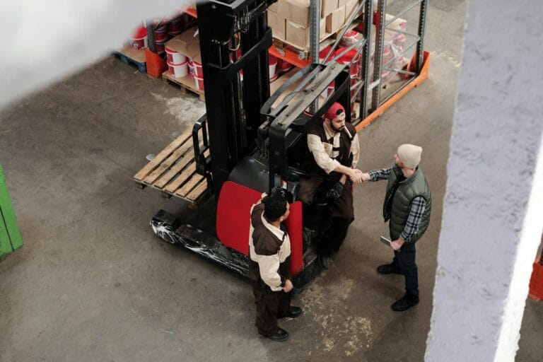 Achieving Balance: The Integration of Racking Systems and Operational Efficiency 1 2026 Three warehouse workers in conversation and handshake next to a forklift in an industrial setting.